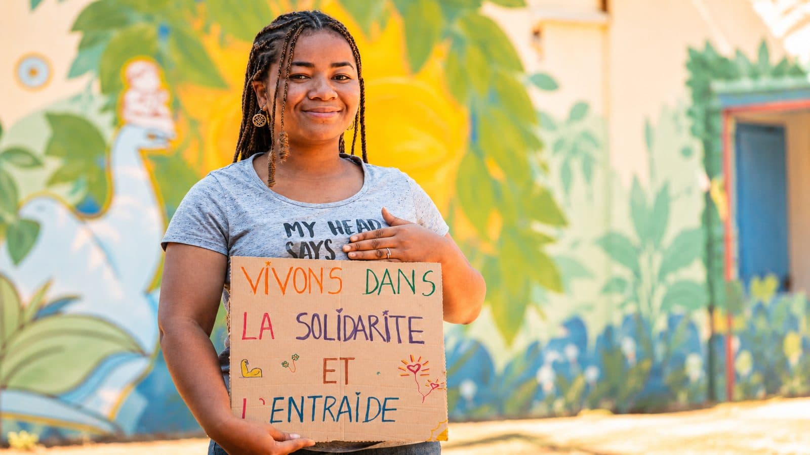 Une femme de l’association tenant une pancarte « Vivons dans la solidarité et l’entraide »