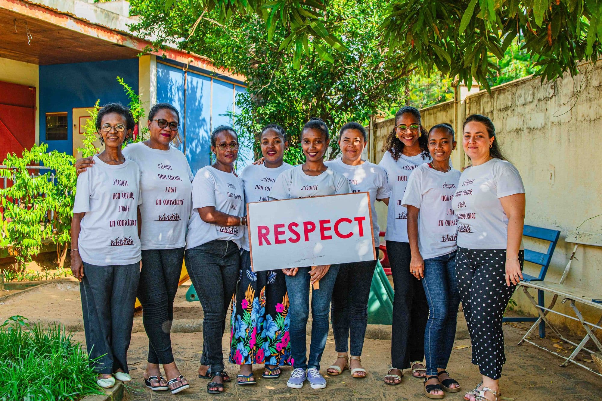 Neuf femmes de l’équipe Cœur et Conscience en t-shirt, souriantes, brandissant une pancarte « RESPECT »